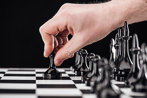 cropped view of man doing move with pawn on chessboard isolated on black