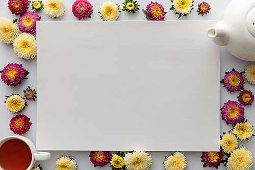 top view of yellow and purple asters and blank paper on white background