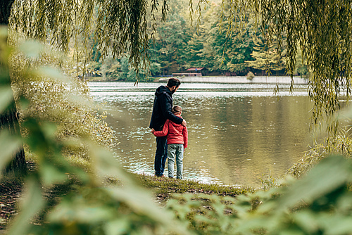 back view of happy father and daughter looking at lake in autumn park