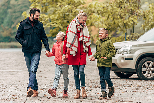 happy young family holding hands while walking together in autumn park