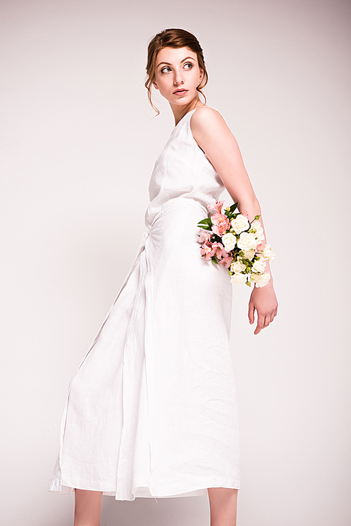beautiful young woman in white dress holding flowers and looking away ...
