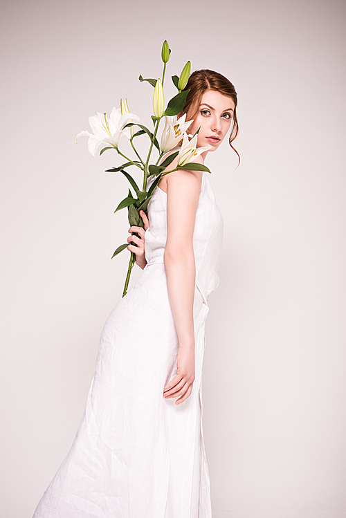 attractive young woman in white dress holding beautiful blooming flowers and  isolated on grey