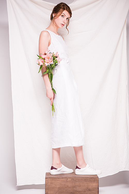 full length view of beautiful young woman in white dress holding tender lilies and 