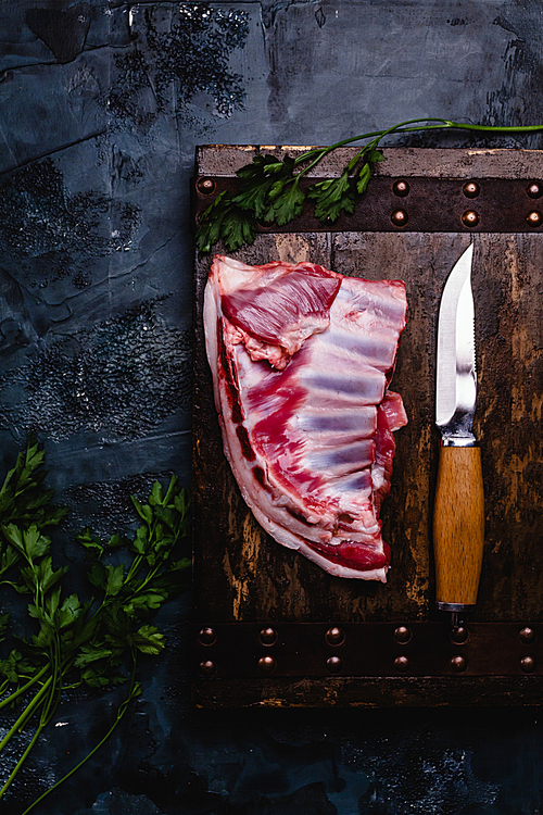 top view of raw beef ribs on wooden board with knife on dark concrete surface