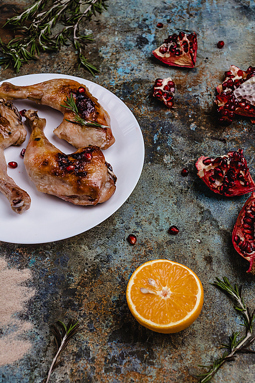 delicious grilled chicken legs with pomegranade seeds and orange on concrete surface