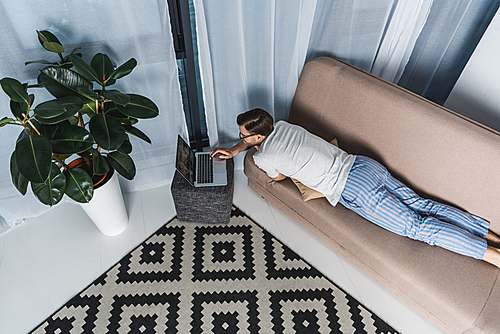 high angle view of freelancer in pajamas working with laptop on couch