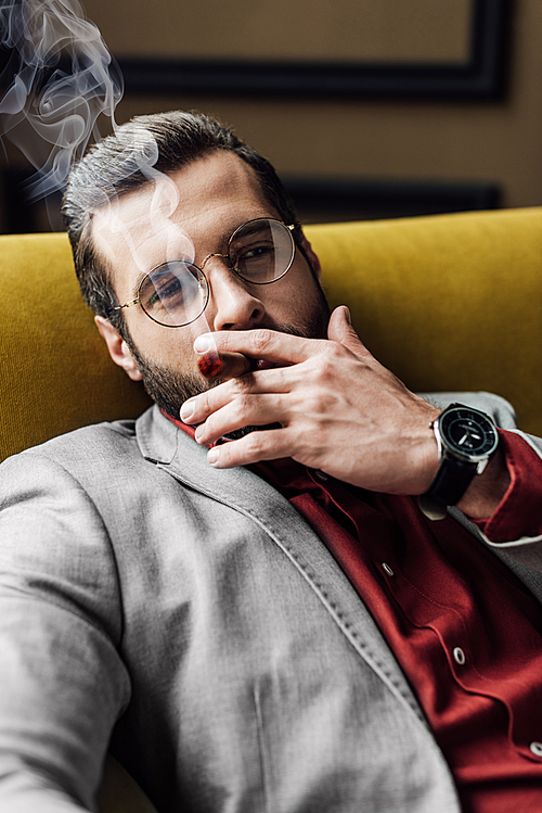 handsome bearded man smoking cigar on couch