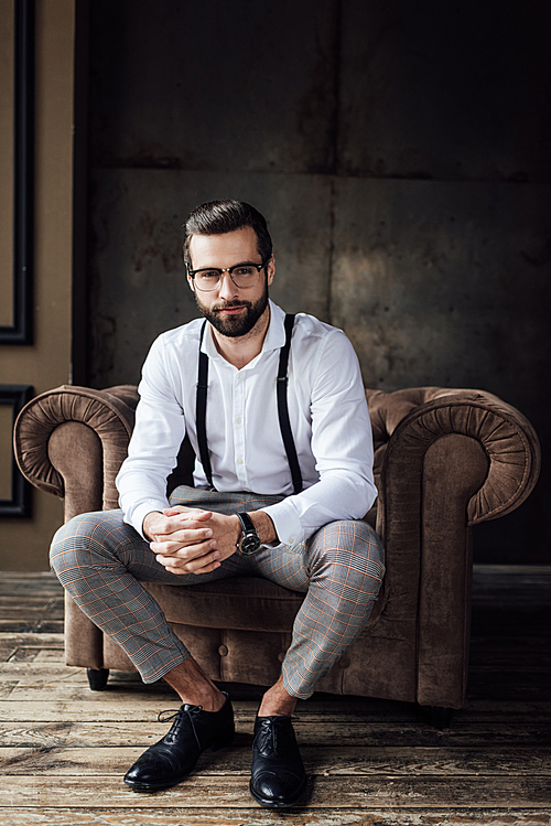 fashionable man in glasses and suspenders sitting in armchair