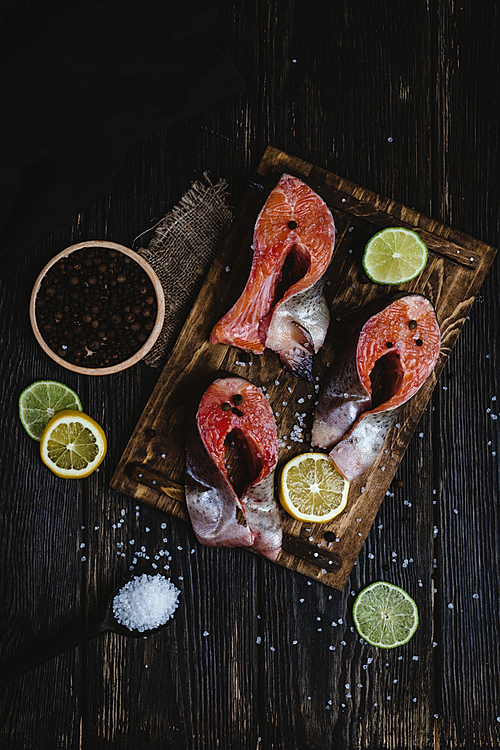 top view of fresh sliced red fish with spices and slices of citrus fruits on rustic wooden table