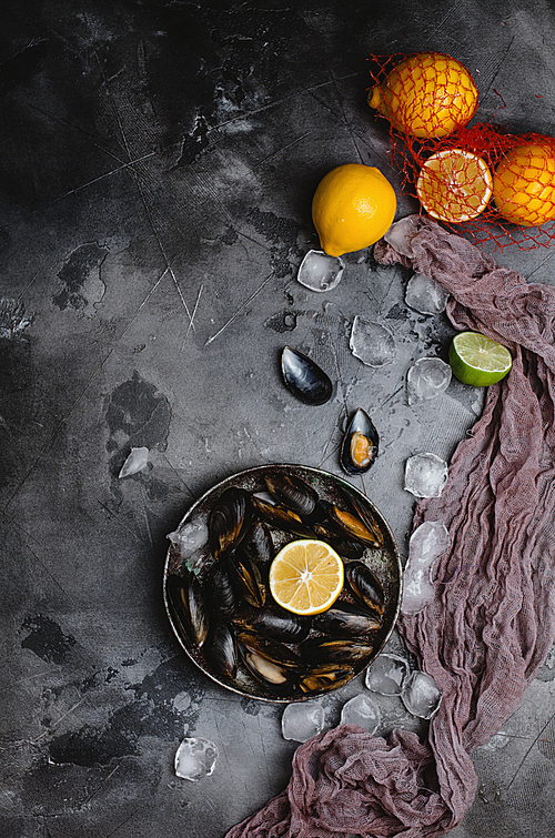 top view of delicious mussels with shells on vintage plate and citrus fruits with ice cubes on grey