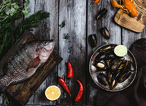 top view of raw fish on cutting board and mussels with lime on rustic wooden table