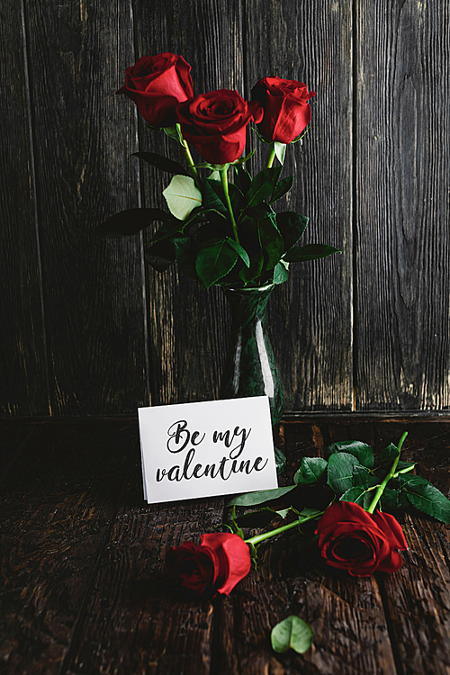 Red roses in vase and Be my valentine card on shabby wooden background