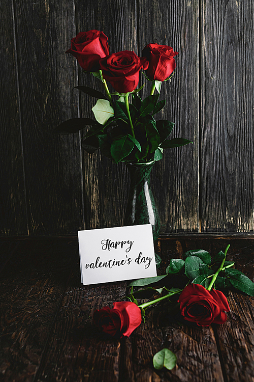 Red roses in vase and Happy valentines day greeting card on shabby wooden background