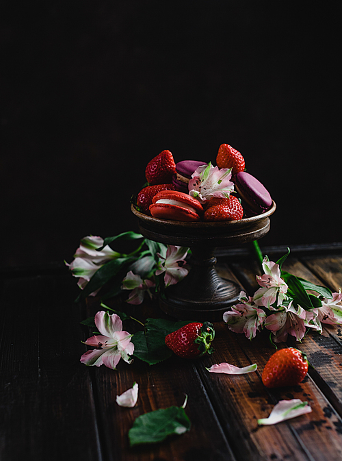 bowl with macarons and strawberries on wooden table with flowers