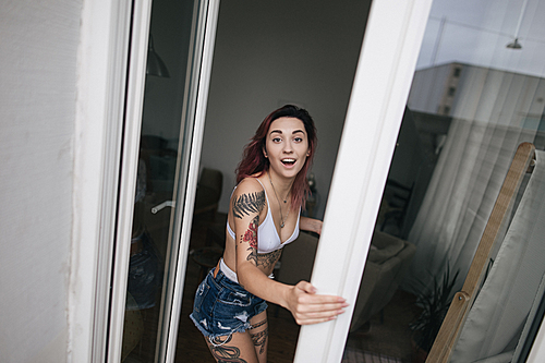 surprised young woman in bra and denim shorts  through open window