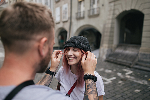 selective focus of man putting hat on beautiful smiling young woman while walking together on street in Bern, Switzerland