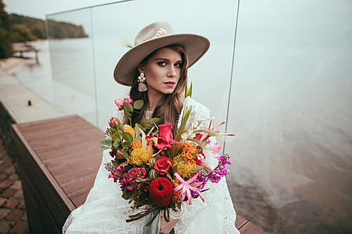 attractive bride in bohemian wedding dress and hat with bouquet