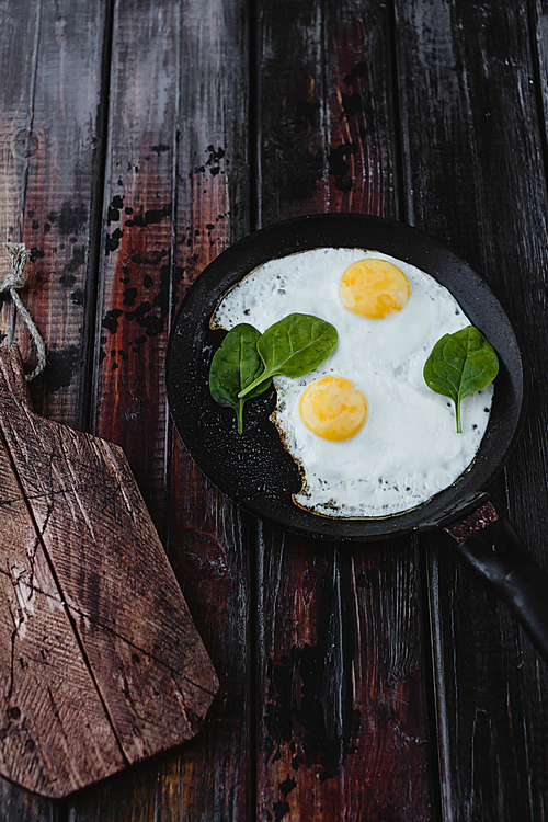 top view of fried eggs with spinach on wooden tabletop