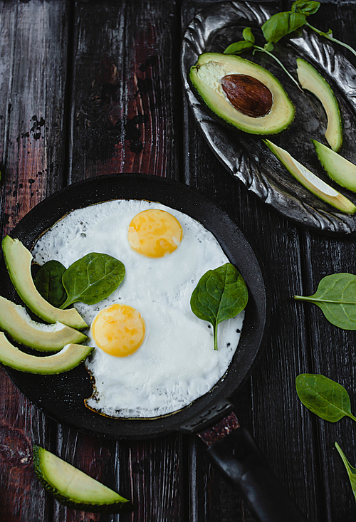 top view of fried eggs with spinach and avocado pieces on wooden tabletop