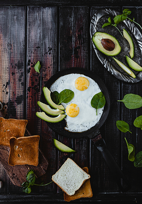 top view of fried eggs with spinach, pieces of avocado and toasts on wooden tabletop