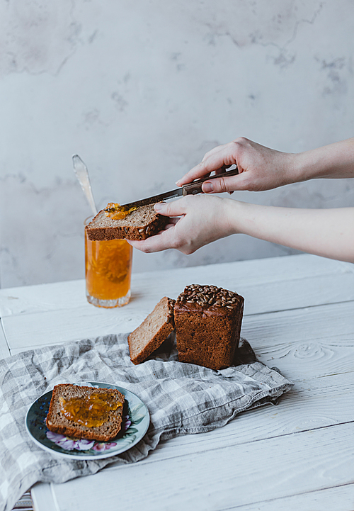 partial view of woman putting jam on piece of bread