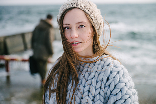 attractive young woman in merino wool sweater and hat on winter seashore