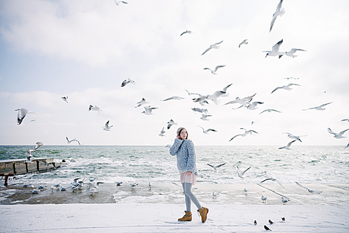 beautiful young girl on winter seashore looking at seagulls