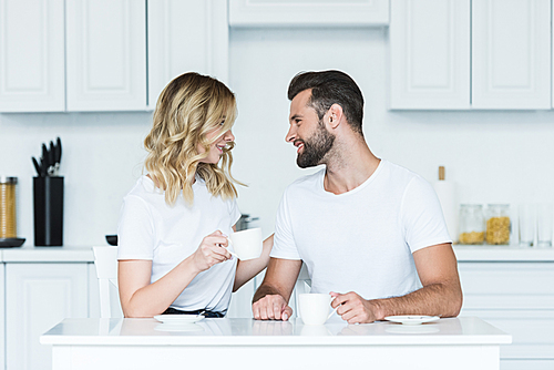 happy young couple drinking coffee and smiling each other in kitchen at morning