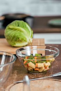 vegetables for salad in bowl, cabbage on cutting board on tabletop in kitchen