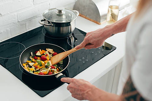 cropped shot of man cooking vegetables in frying pan on electric stove