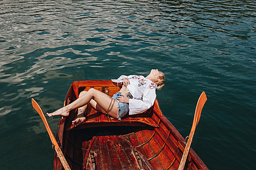 high angle view of young woman relaxing in wooden boat on lake
