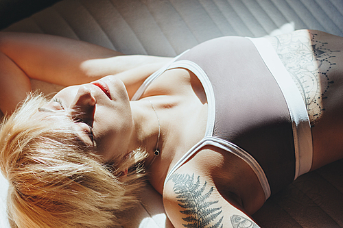 close-up view of beautiful young woman with tattoos wearing underwear and resting at sunlight