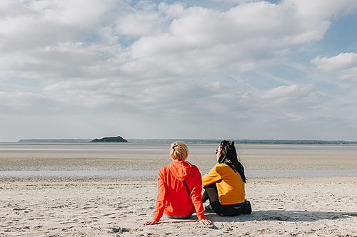 back view of girls sitting on sandy beach, Saint michaels mount, Normandy, France