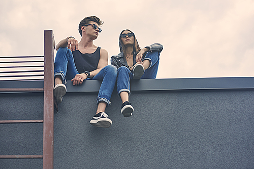 bottom view of interracial young couple in sunglasses sitting on roof