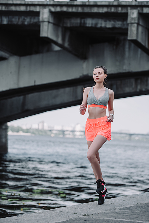 attractive sportswoman jogging on quay near bridge