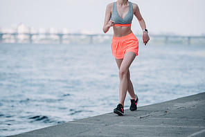 cropped view of sportswoman jogging quay near river