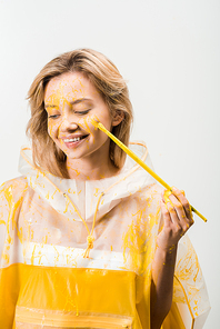 beautiful woman in raincoat painting face with yellow paint and looking down isolated on white