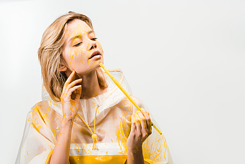 beautiful woman in raincoat painting face with yellow paint isolated on white