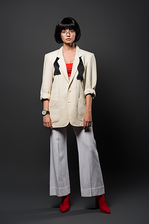 fashionable young woman in stylish jacket and bell-bottoms on grey