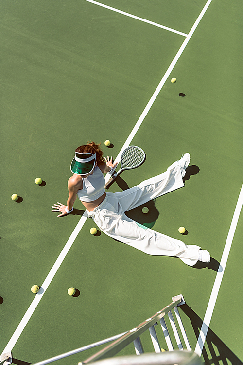 high angle view of beautiful woman in stylish white clothing sitting on tennis court with balls and racket around