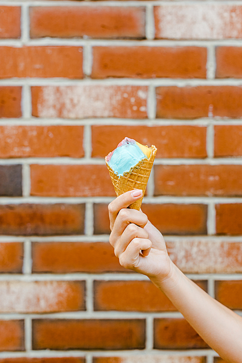 cropped shot of woman holding ice cream in waffle cone in front of brick wall