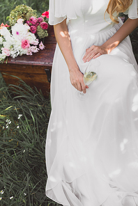 cropped shot of bride holding glass of champagne and sitting on vintage chest
