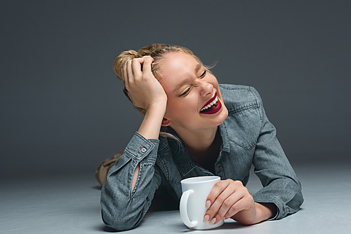beautiful laughing girl with cup of coffee lying on grey