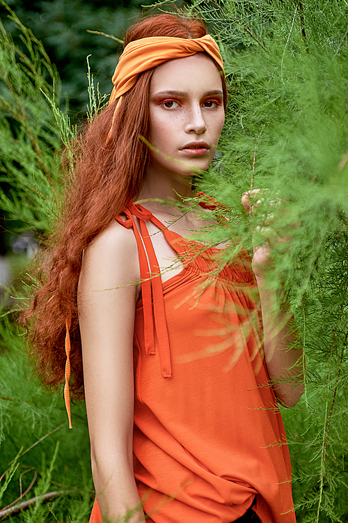 attractive fashionable girl in orange headband posing at green plant