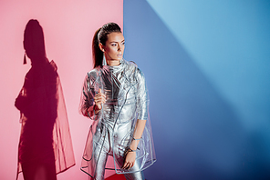 beautiful girl posing in metallic bodysuit and trendy raincoat on pink and blue background
