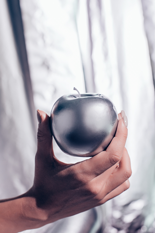 cropped view of girl holding silver apple in hand on metallic background