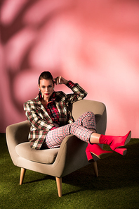 beautiful elegant girl in checkered suit posing in armchair on pink background