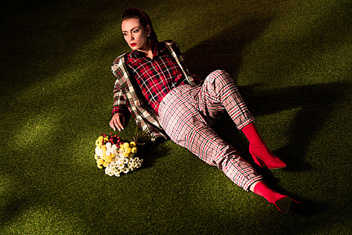 fashionable girl in warm checkered suit posing with bouquet of flowers on green carpet