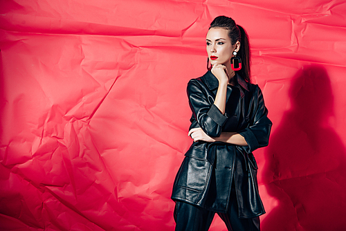 fashionable young woman posing in black leather suit on red background