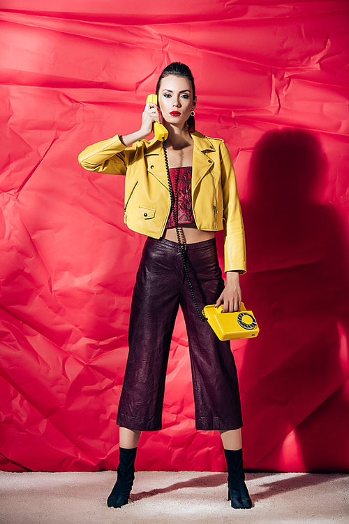 young woman in yellow leather jacket talking on retro phone on red background